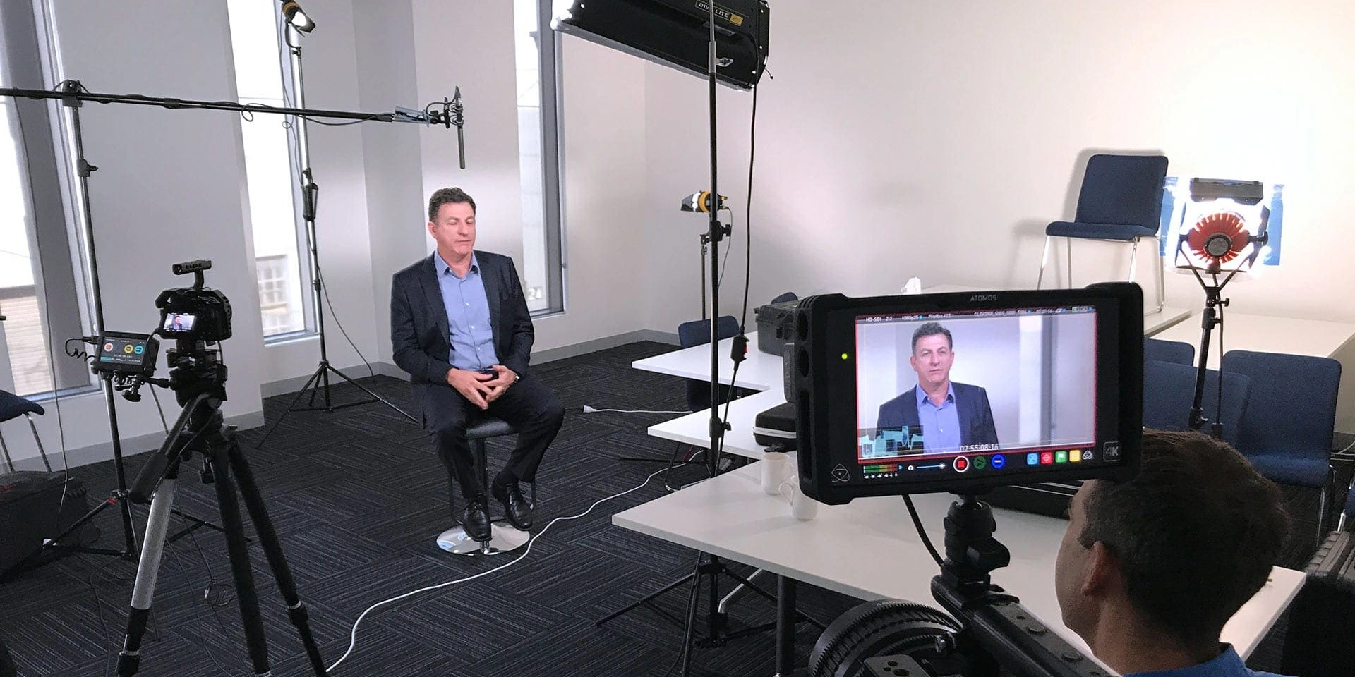 Two people in a Sydney office film a recruitment video, with a camera on a tripod facing a smiling team member who speaks to the lens.